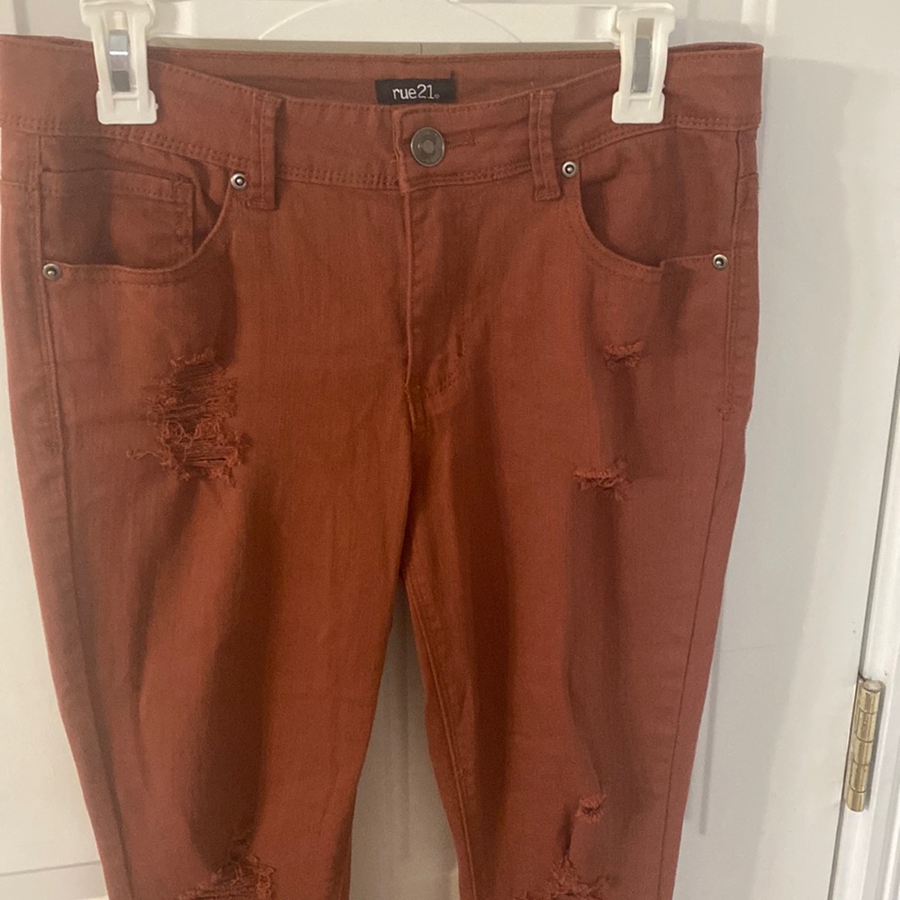 women’s mid m-rise rust colored jeans with ripped detailing on front and ankles